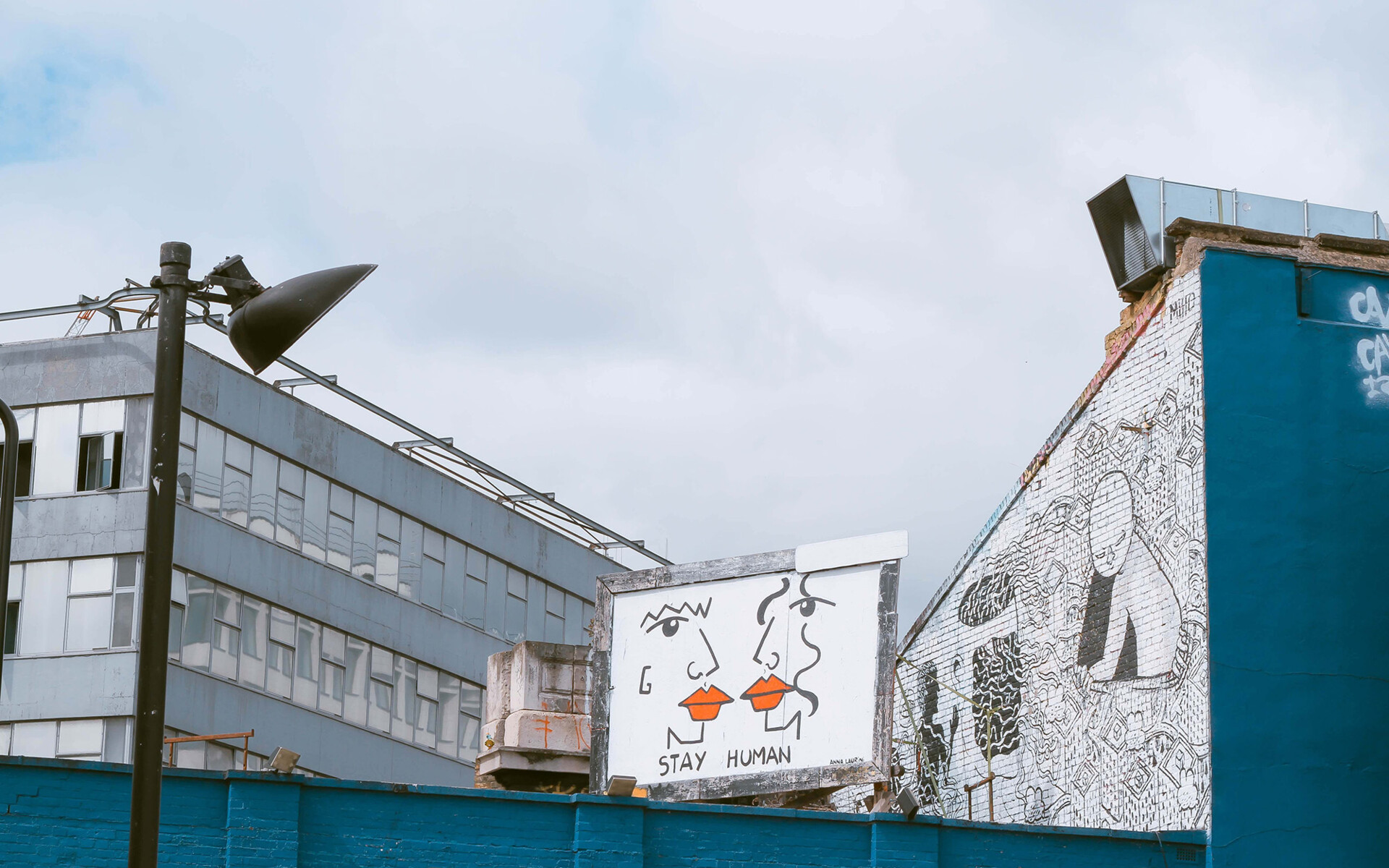Titelbild bei politischbilden.de: ein altes Industriegebäude mit einem Graffiti mit sich küssenden Gesichtern